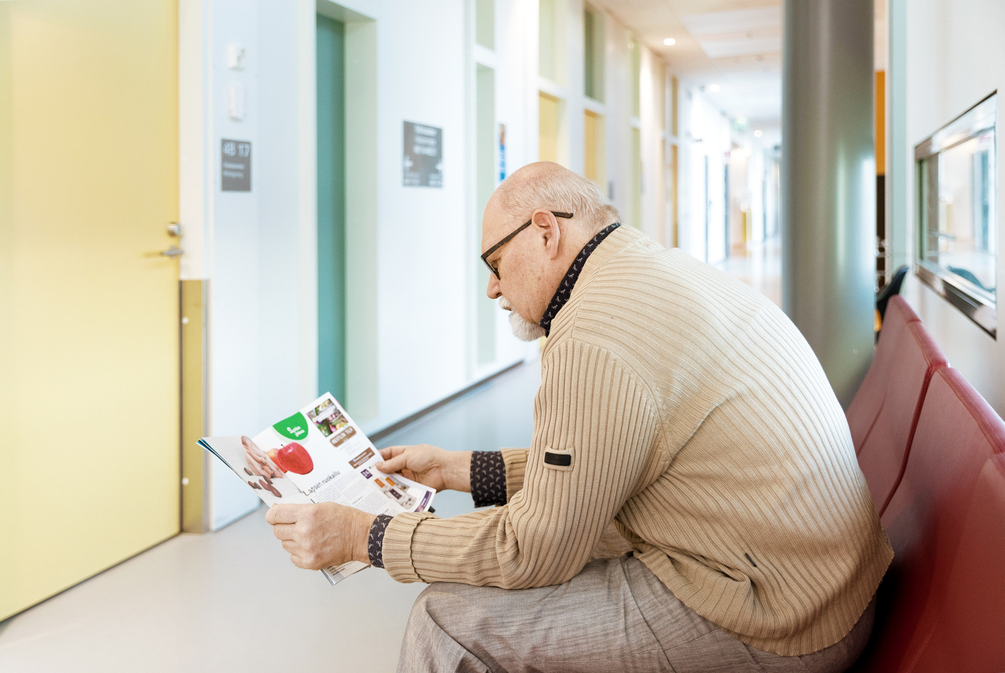 En äldre man sitter i väntrummet på hälsovårdscentralen och läser en tidning.