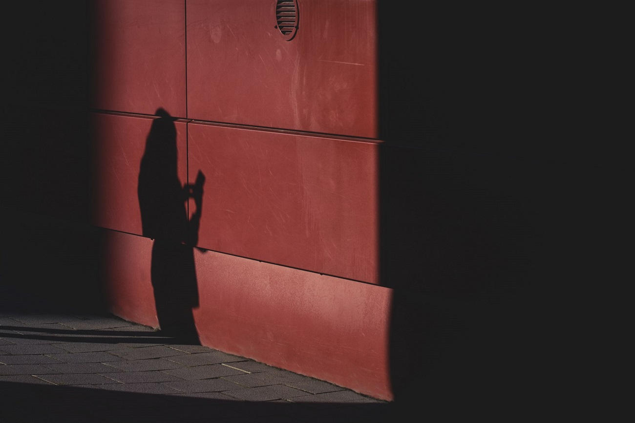 Skuggan av en person som använder en telefon mot en röd vägg.
