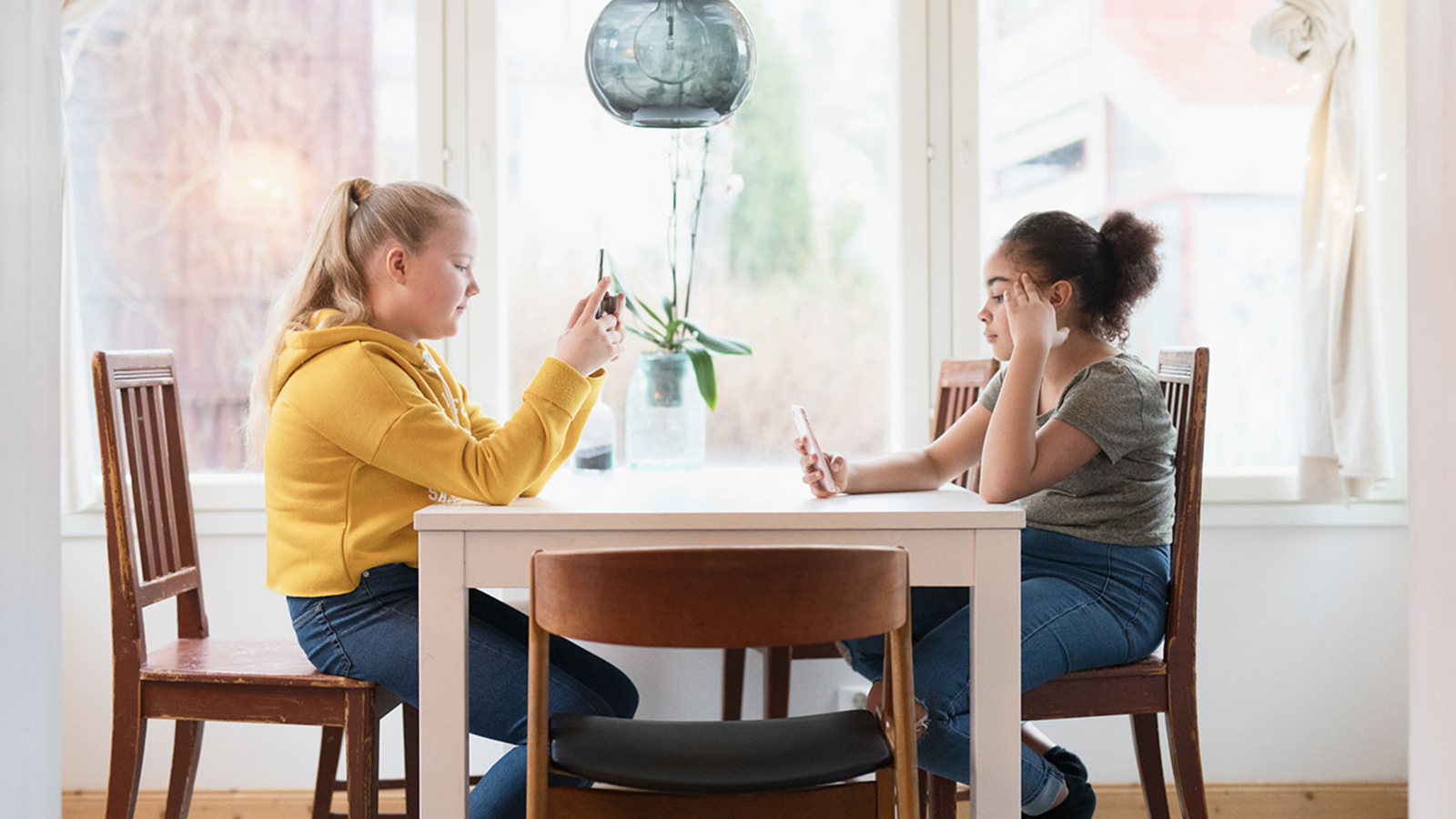 Kaksi tyttöä istuu pöydän ääressä ja katselee puhelimia