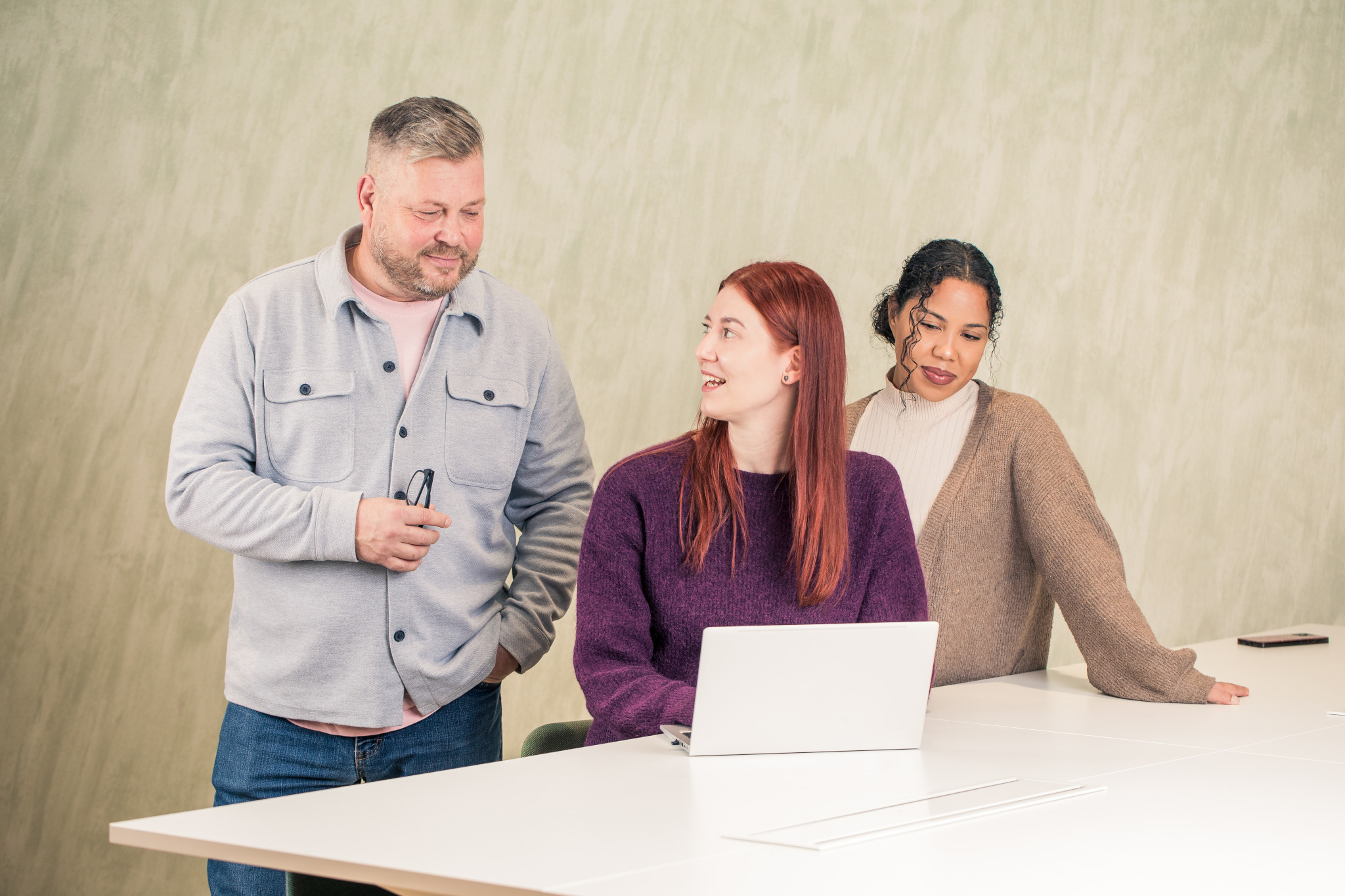 På bilden sitter tre personer på sin arbetsplats vid ett bord och tittar på något på en dator.