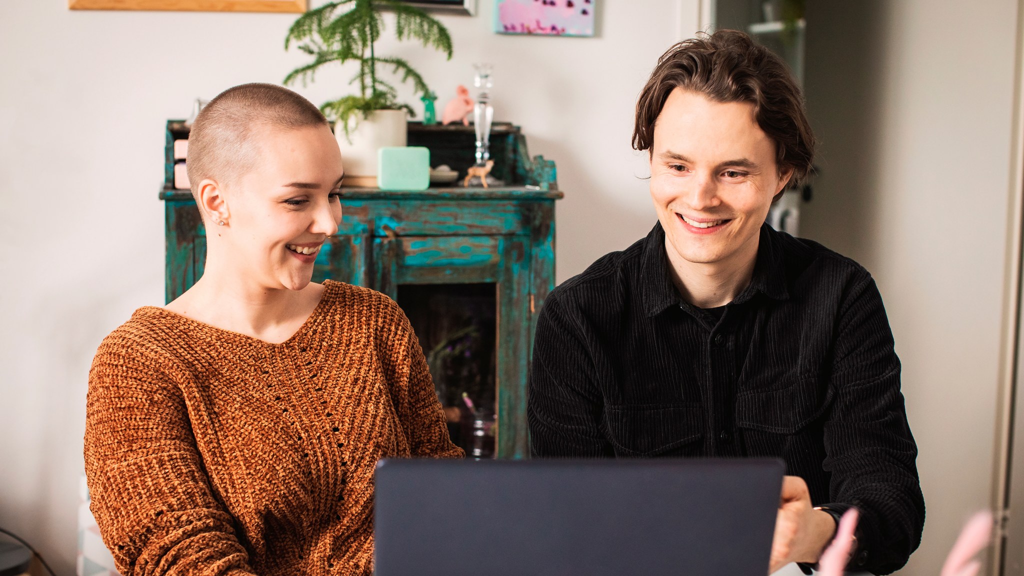 A young woman and man are looking at a laptop and smiling.