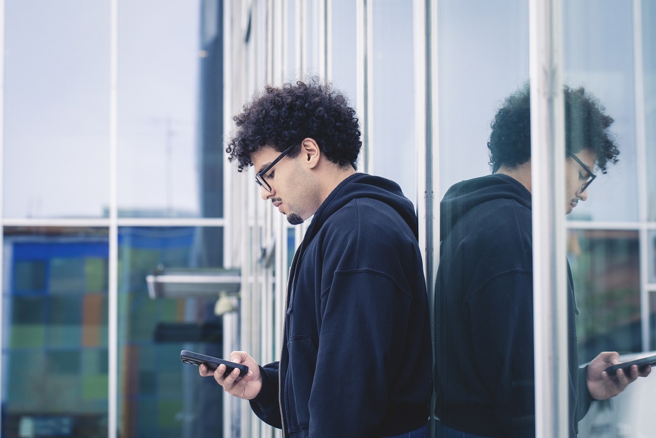 Nuori henkilö seisoo ulkona ja katselee puhelintaan.